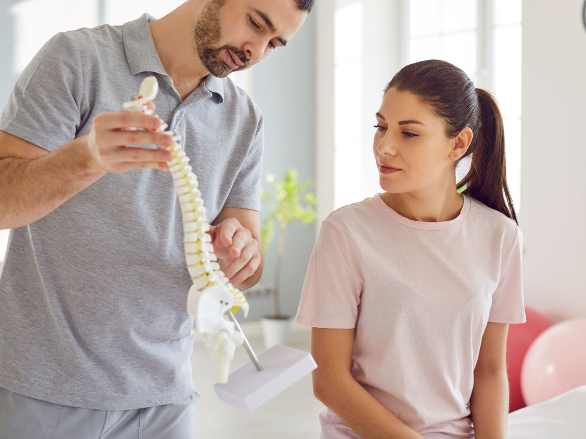 A healthcare professional explaining spinal anatomy to a patient using a model of a spine.